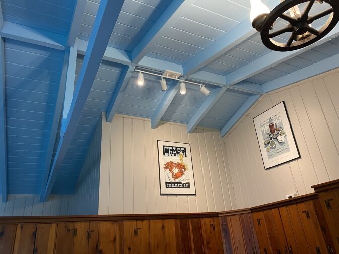 Light blue vaulted ceiling above wood-paneled walls, with two framed posters hanging on the tan wall. A black wagon wheel light fixture is partly visible in the upper right corner.