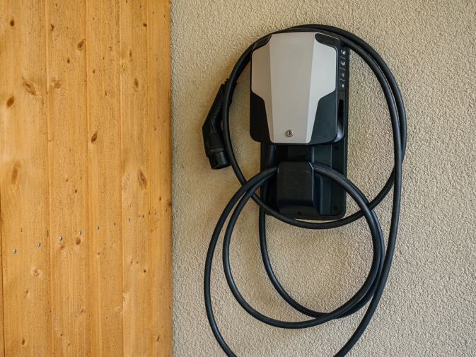 Electric vehicle charging station mounted on a textured wall with a coiled charging cable hanging neatly below the device.
