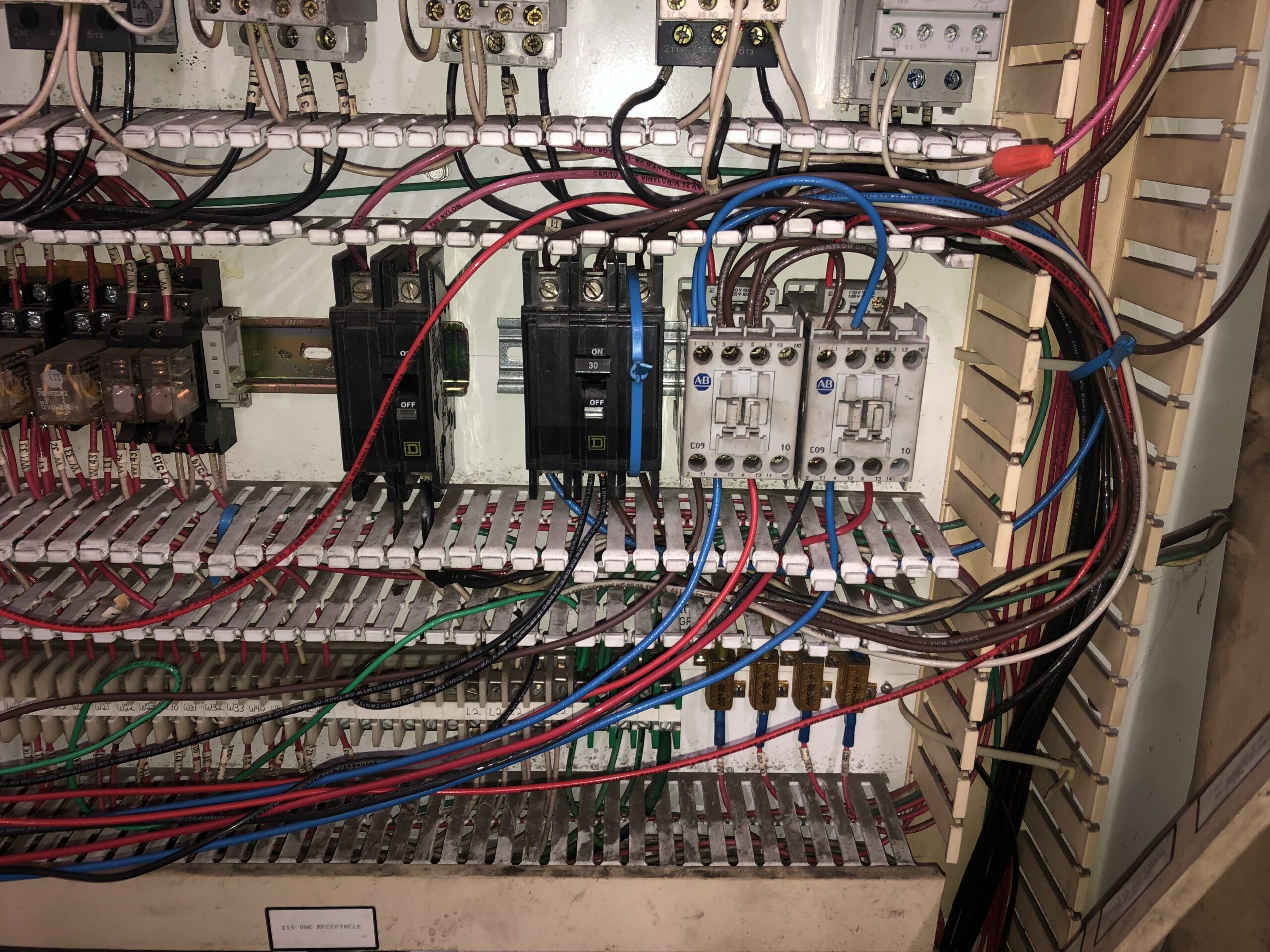 Electrical control panel with various wires, relays, fuses, and circuit breakers connected, showing organized yet densely packed wiring and components.